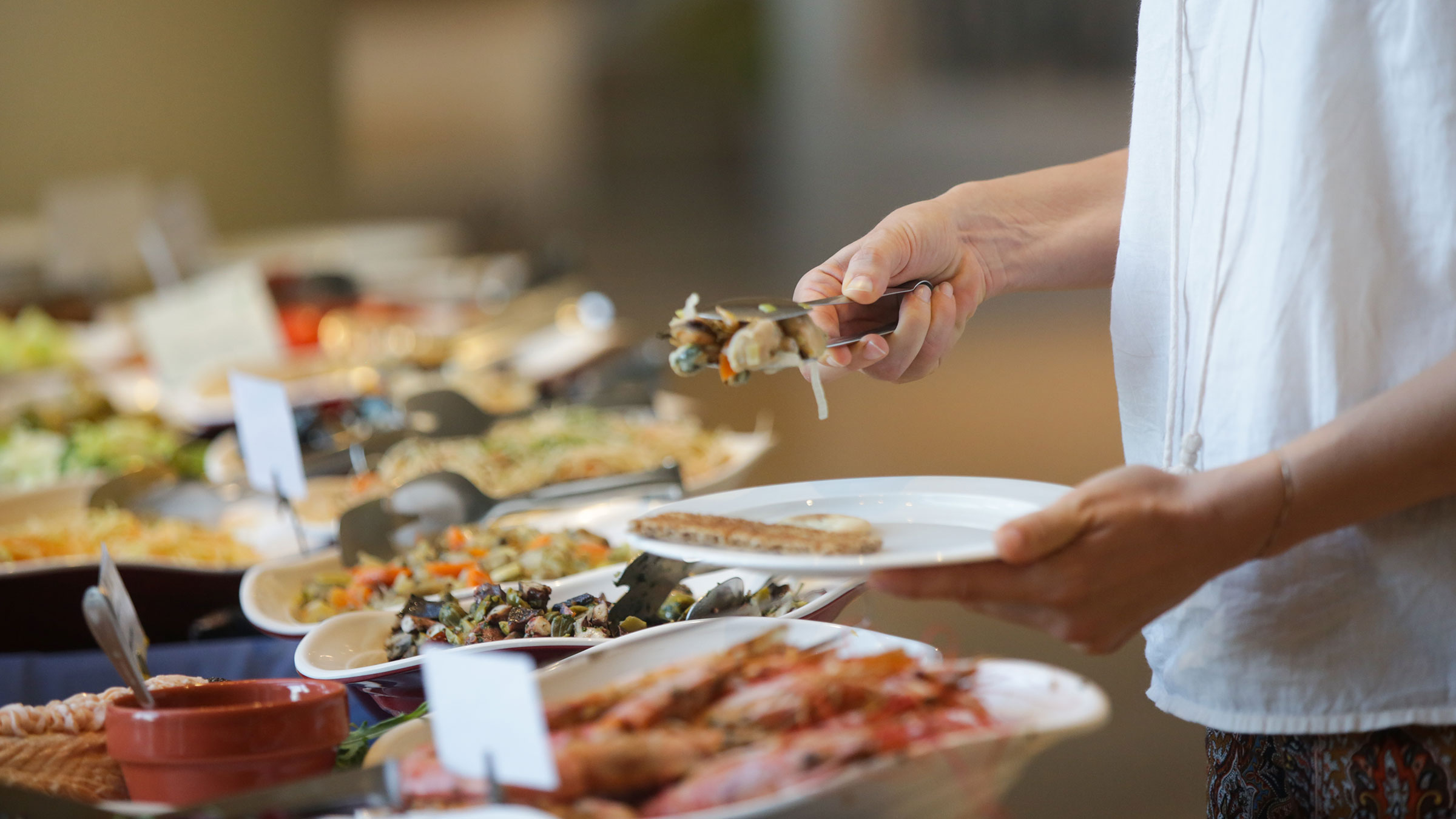 Woman taking food from a buffet line with dishes labelled