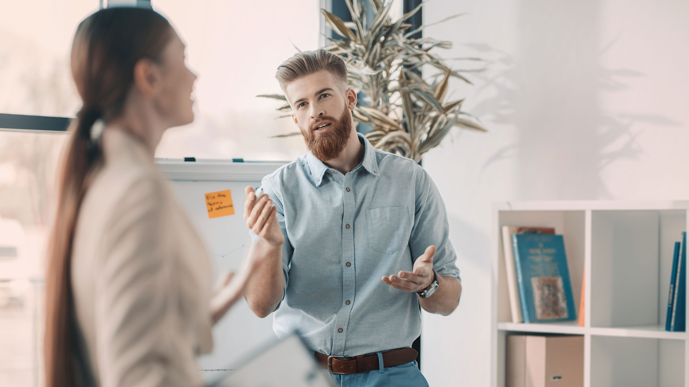 Young bearded businessman gesturing and looking at colleague