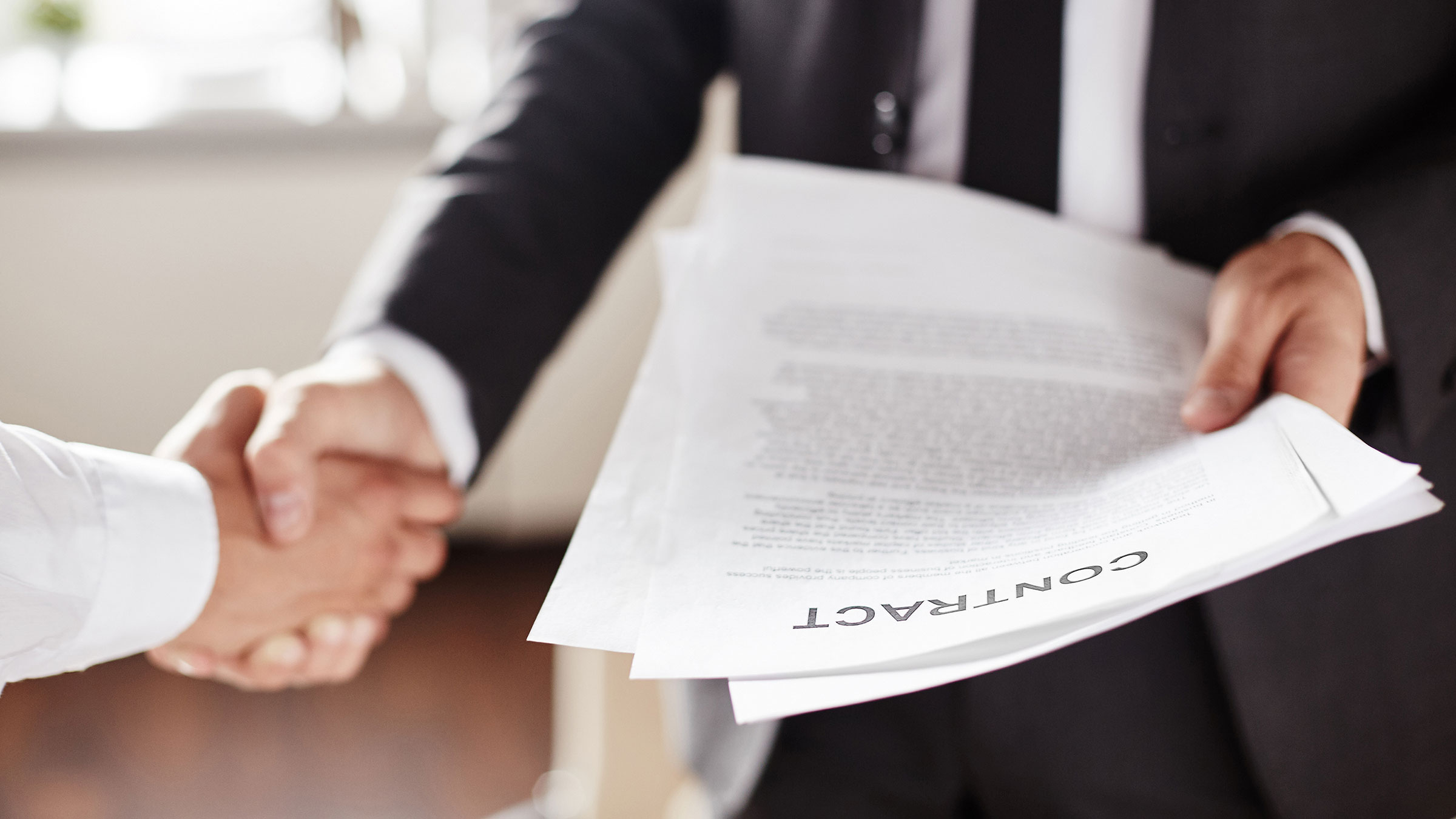 Business contract held by businessman during handshake with partner