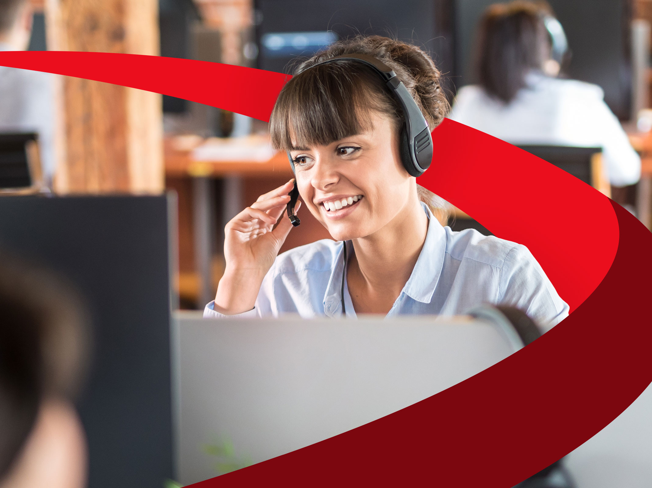 A customer care professional speaking into a headset and smiling. She is in an office setting.