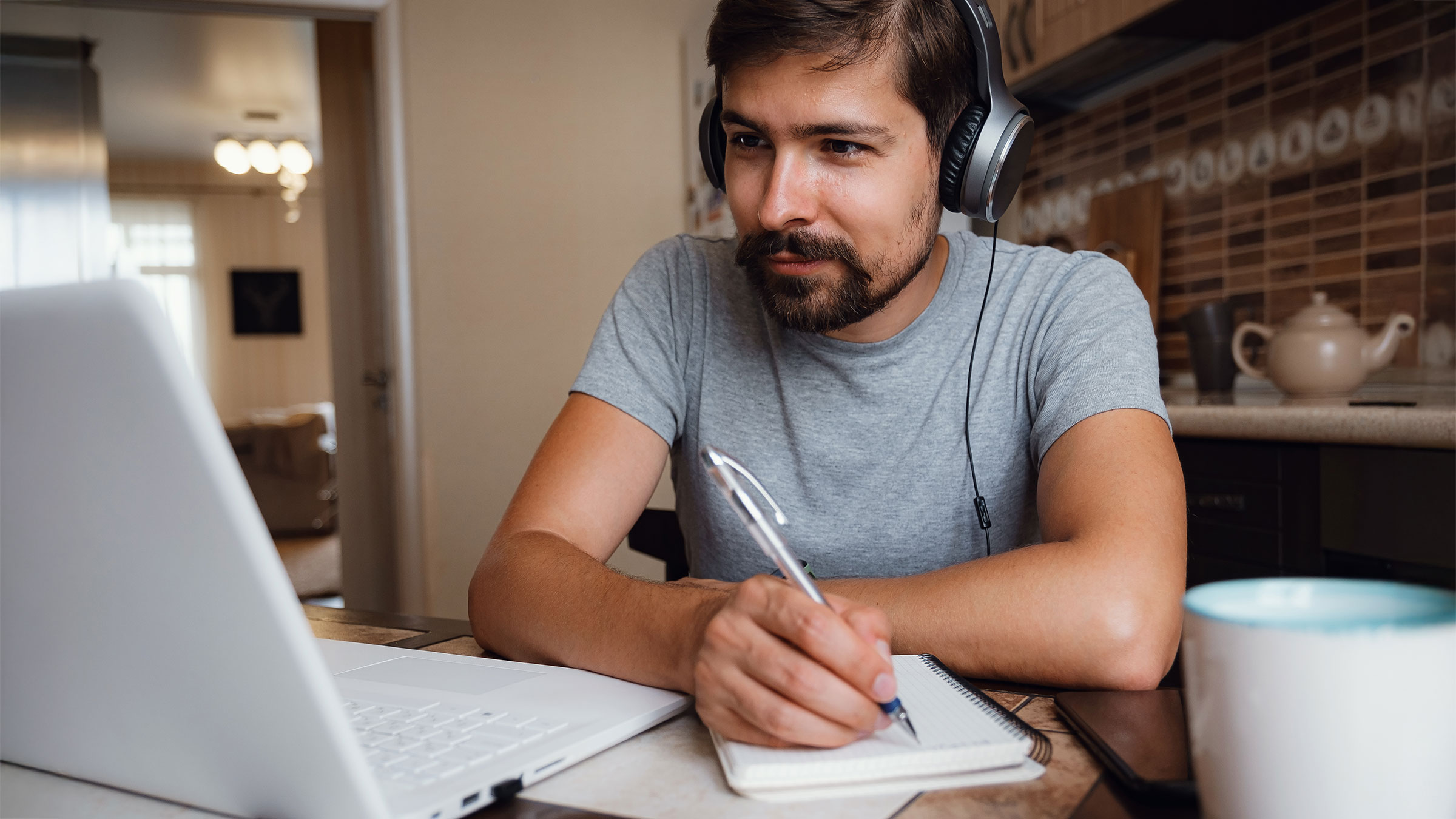 Focused young man wearing headphones watching training on laptop and taking notes