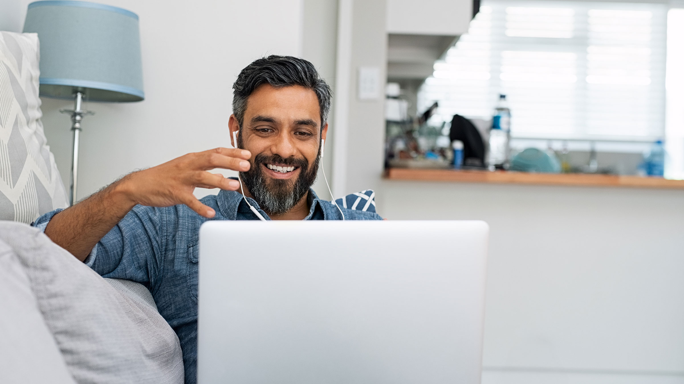 Man sitting on couch at home interacting with trainer on laptop