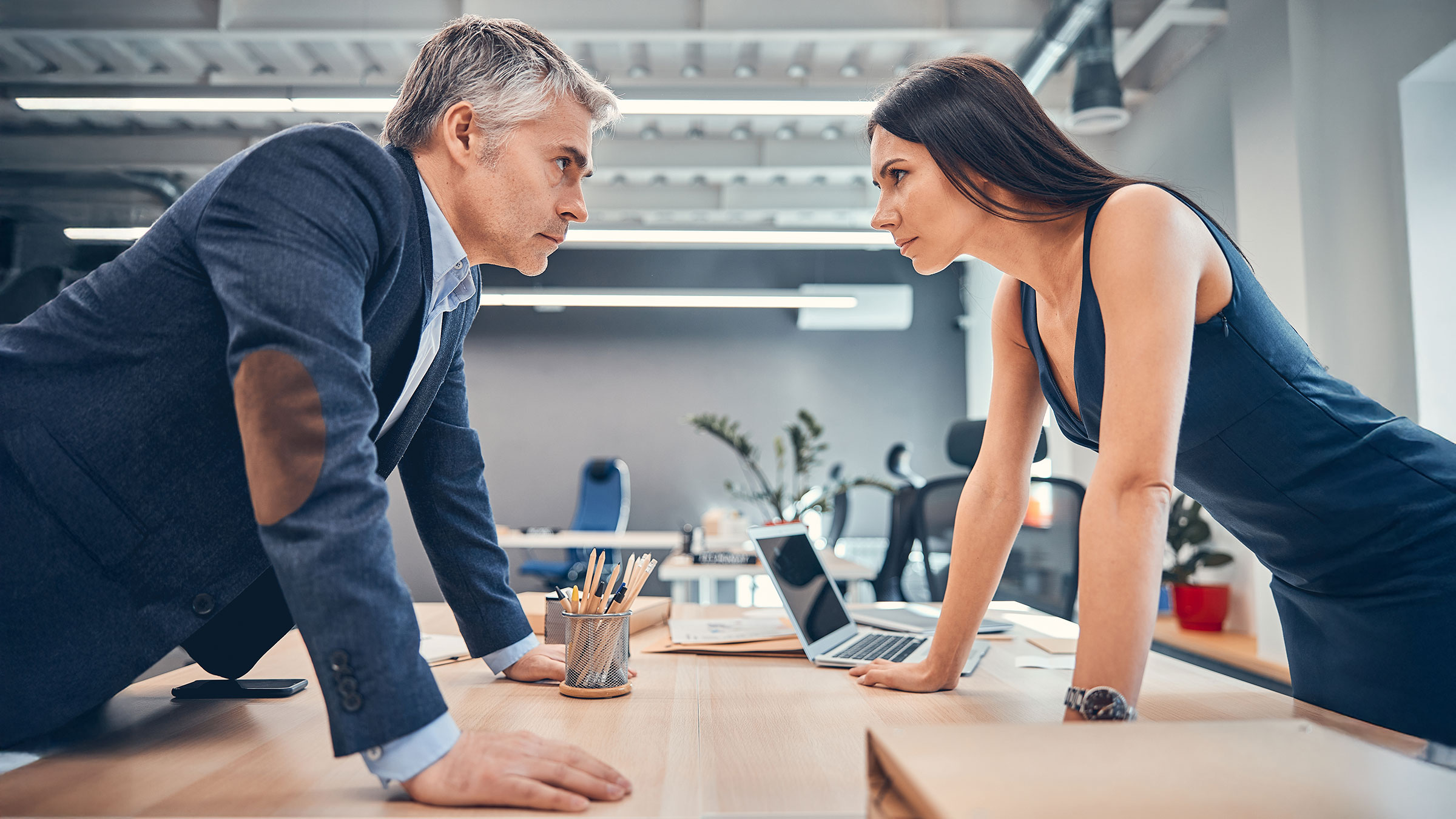 Angry boss with colleague standing and staring eye-to-eye across a table