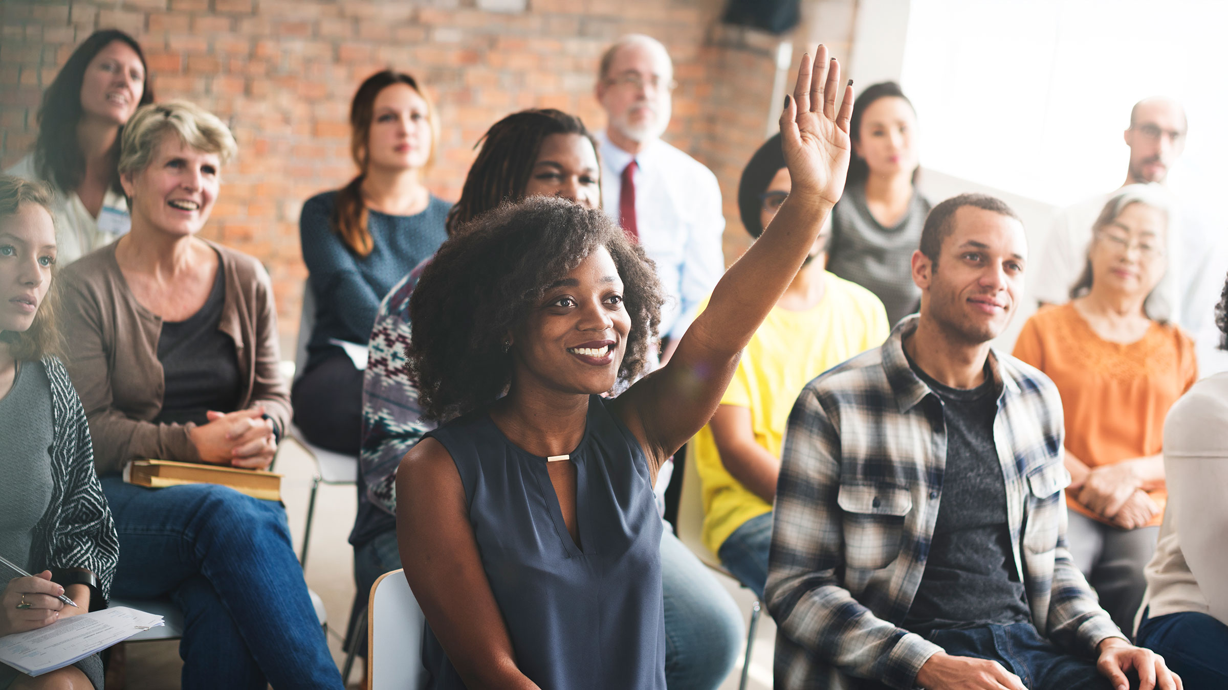 Woman raising her hand in meeting of diverse group of employees
