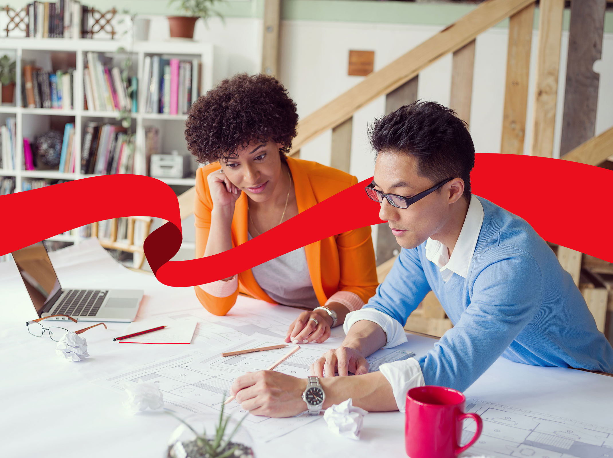 Two business professionals sitting at a table in an office setting. They are strategically working on a document and a laptop.