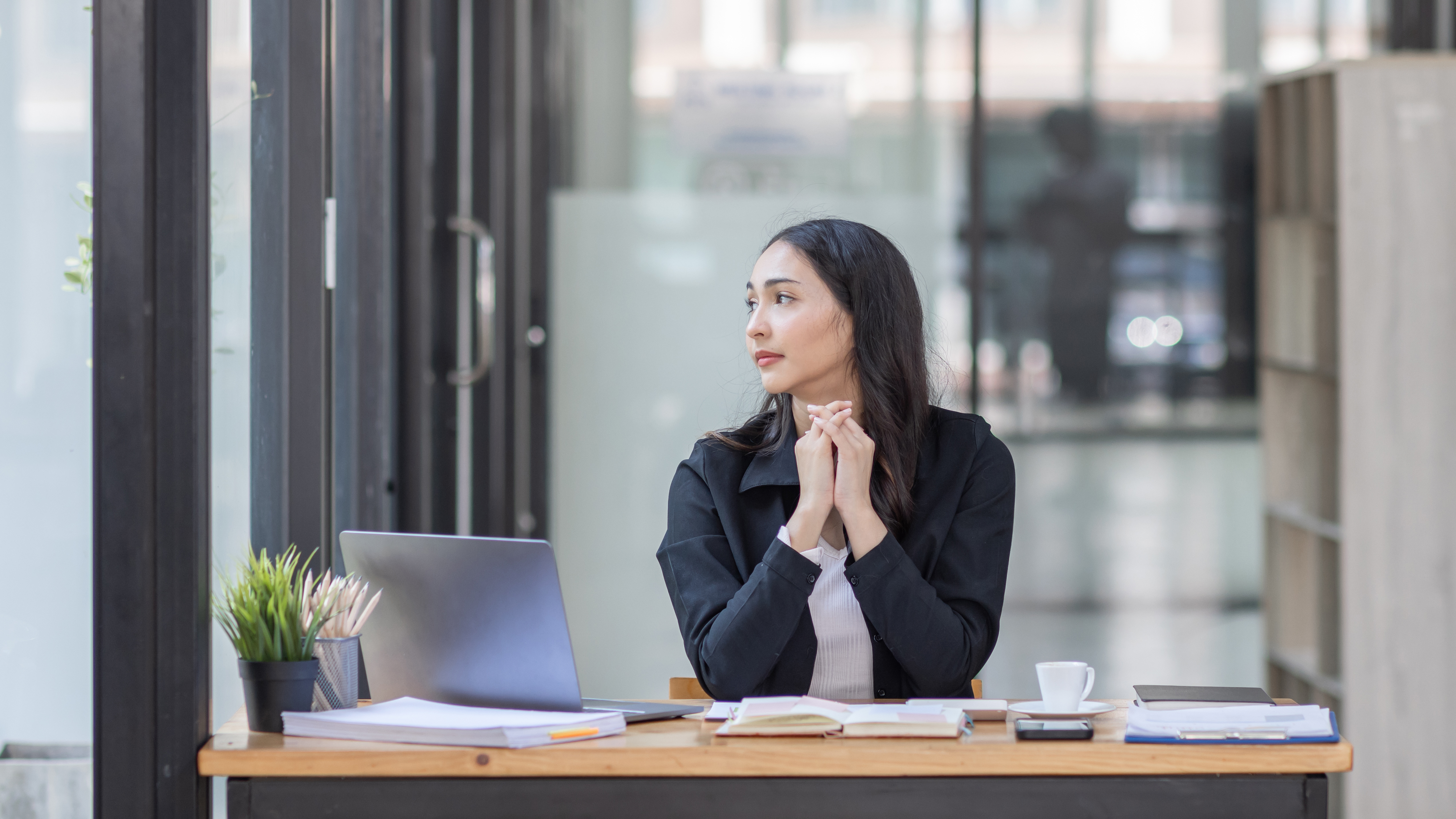Woman at a desk staring out a window thinking