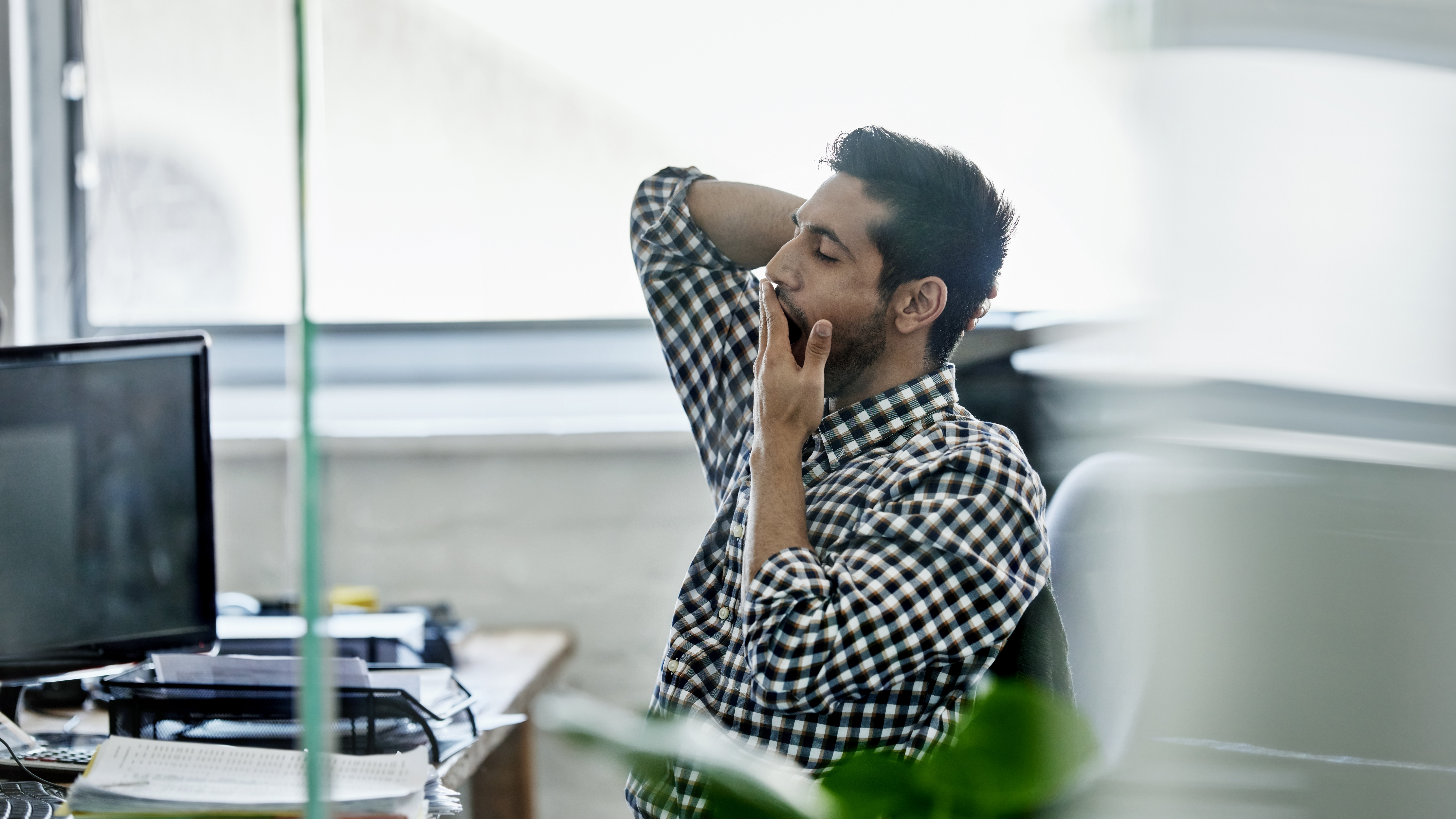 A man seated at a desk, yawning