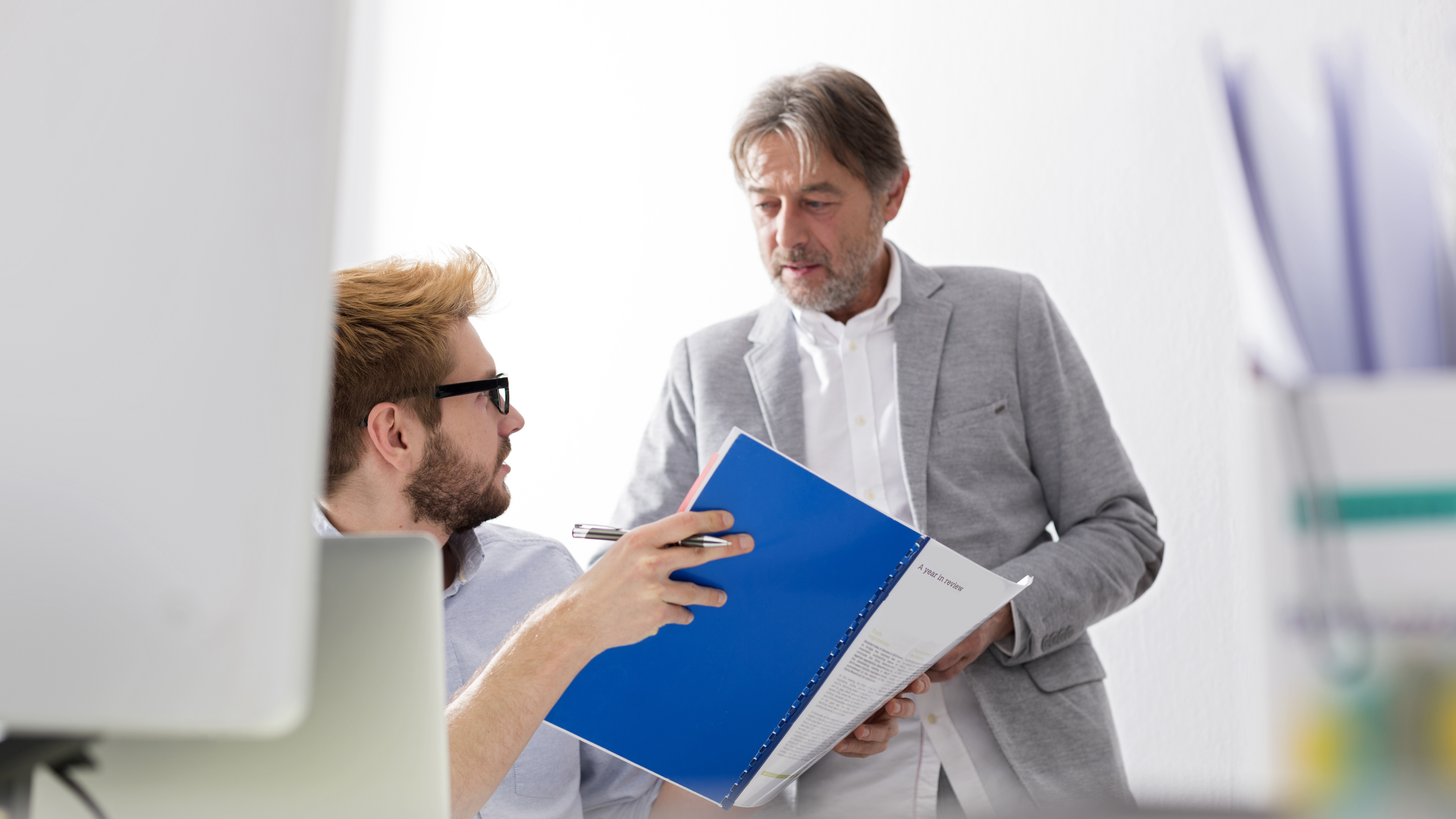A manager talking to a younger employee who is holding a report