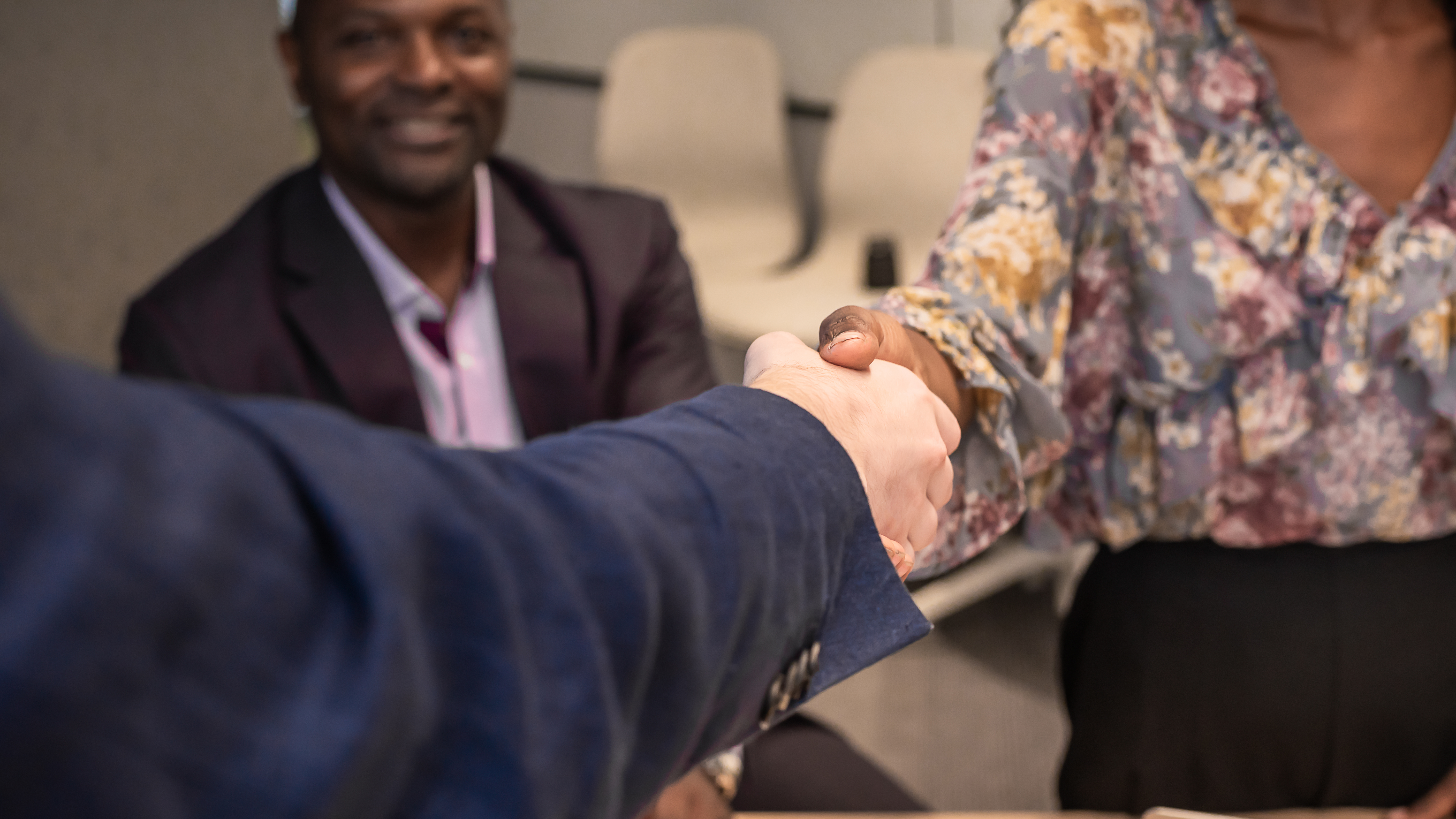 Two people shaking hands while a man looks on
