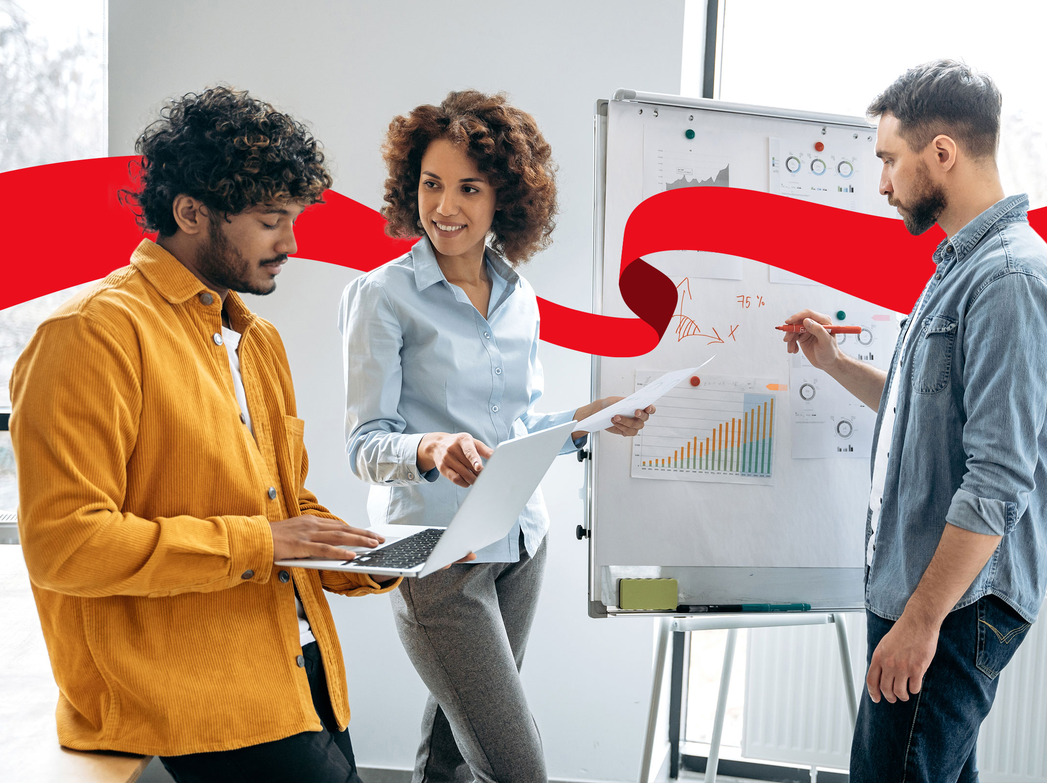 Three marketing professionals reviewing information on a whiteboard and on a laptop. They are in an office setting.