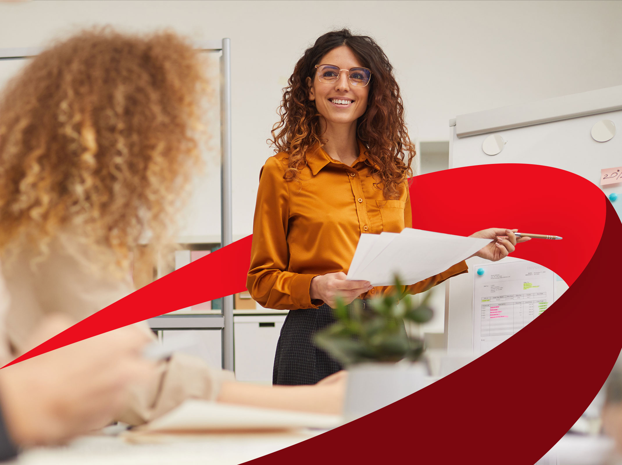A business professional communicating with others in front of a white board. She is hold some papers and in smiling in a business setting.
