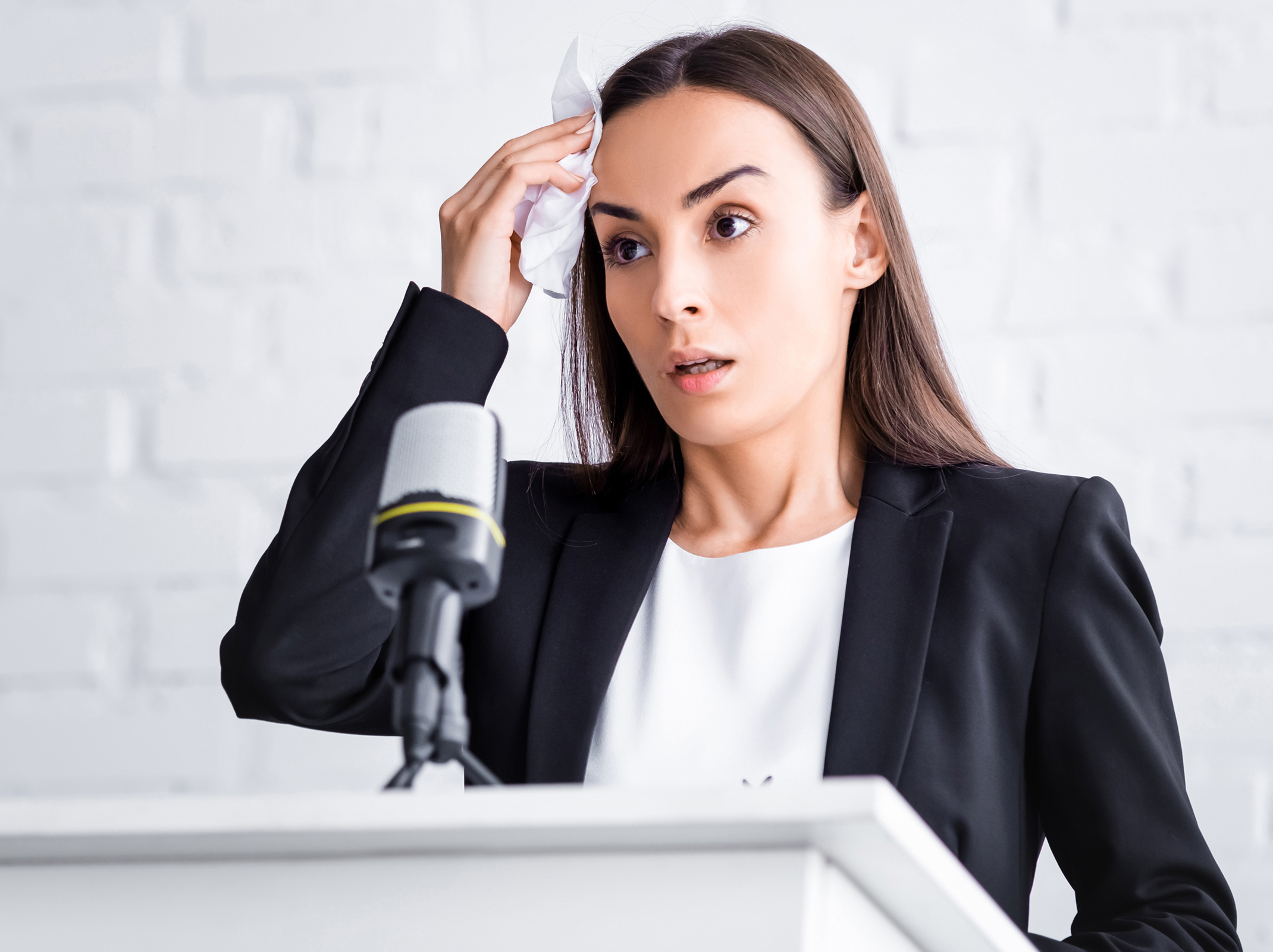 nervous woman in suit standing at podium wiping her forehead with a cloth
