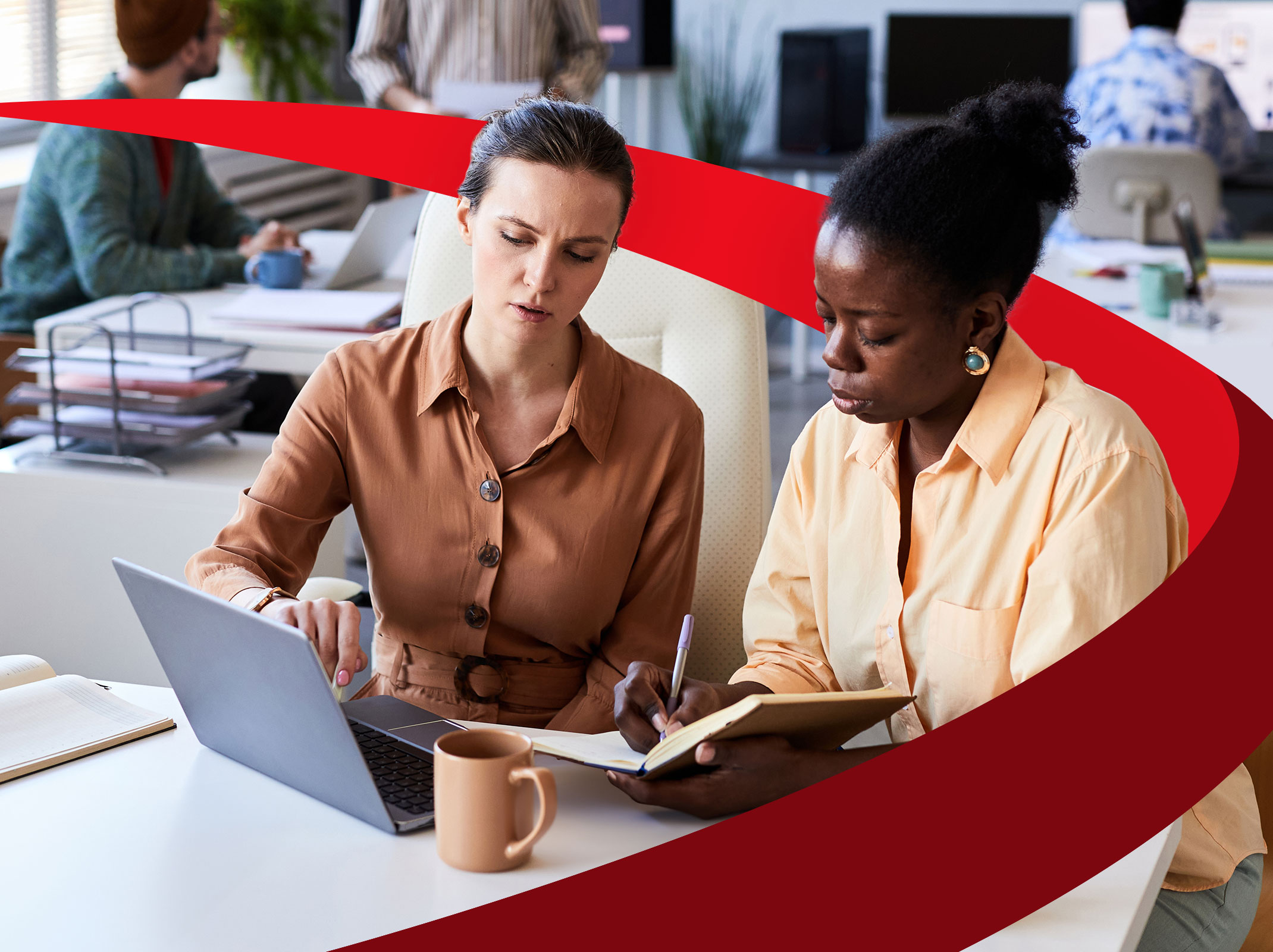 A business leaders is presenting something to another business professional on her laptop. The second professional is taking notes in a notebook.