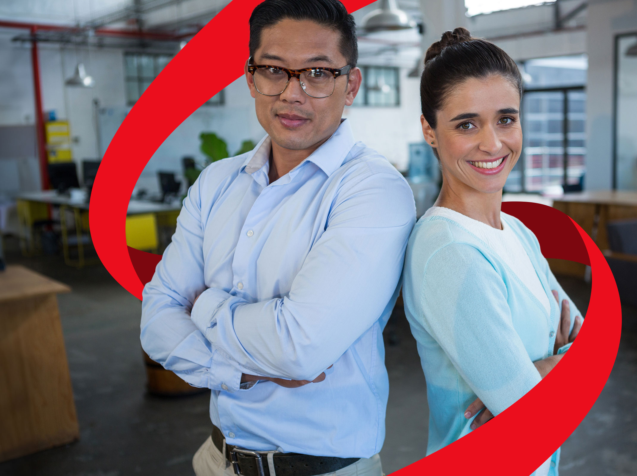 Two business professionals standing back to back in an office setting. They are smiling.