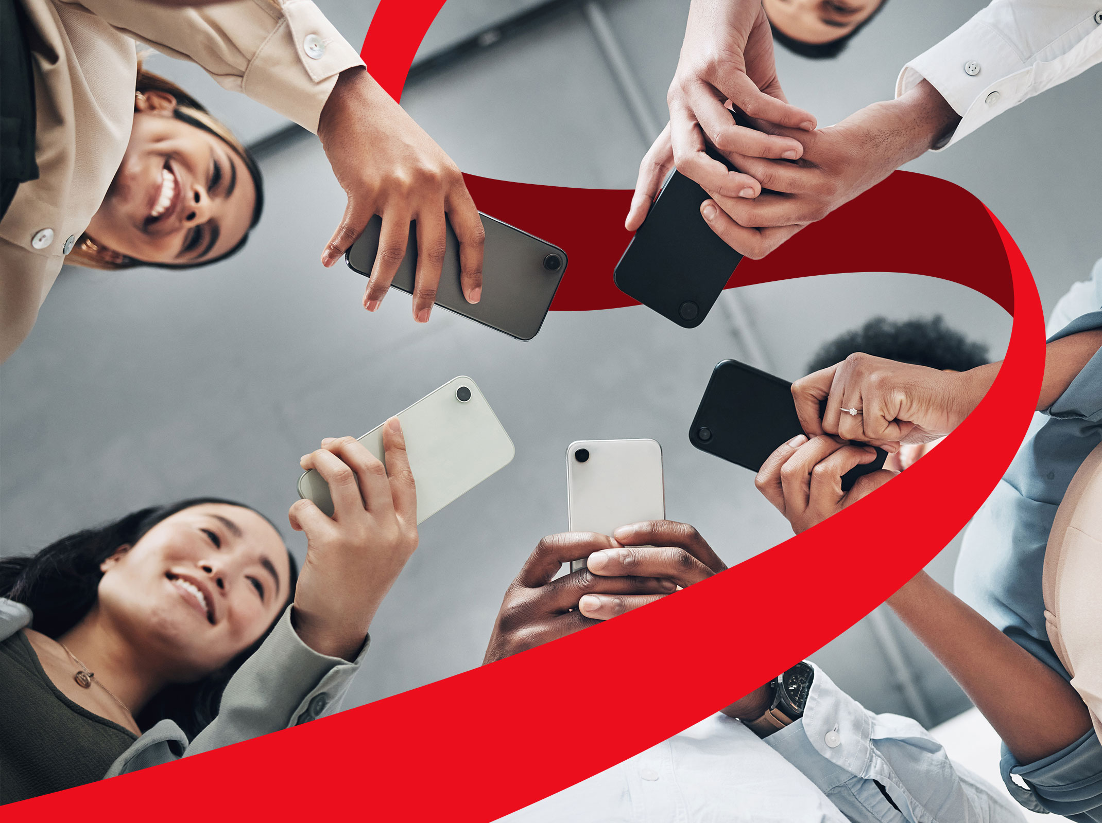 A group of business professionals using their phones to view social media. The image is looing up on the smiling business professionals.