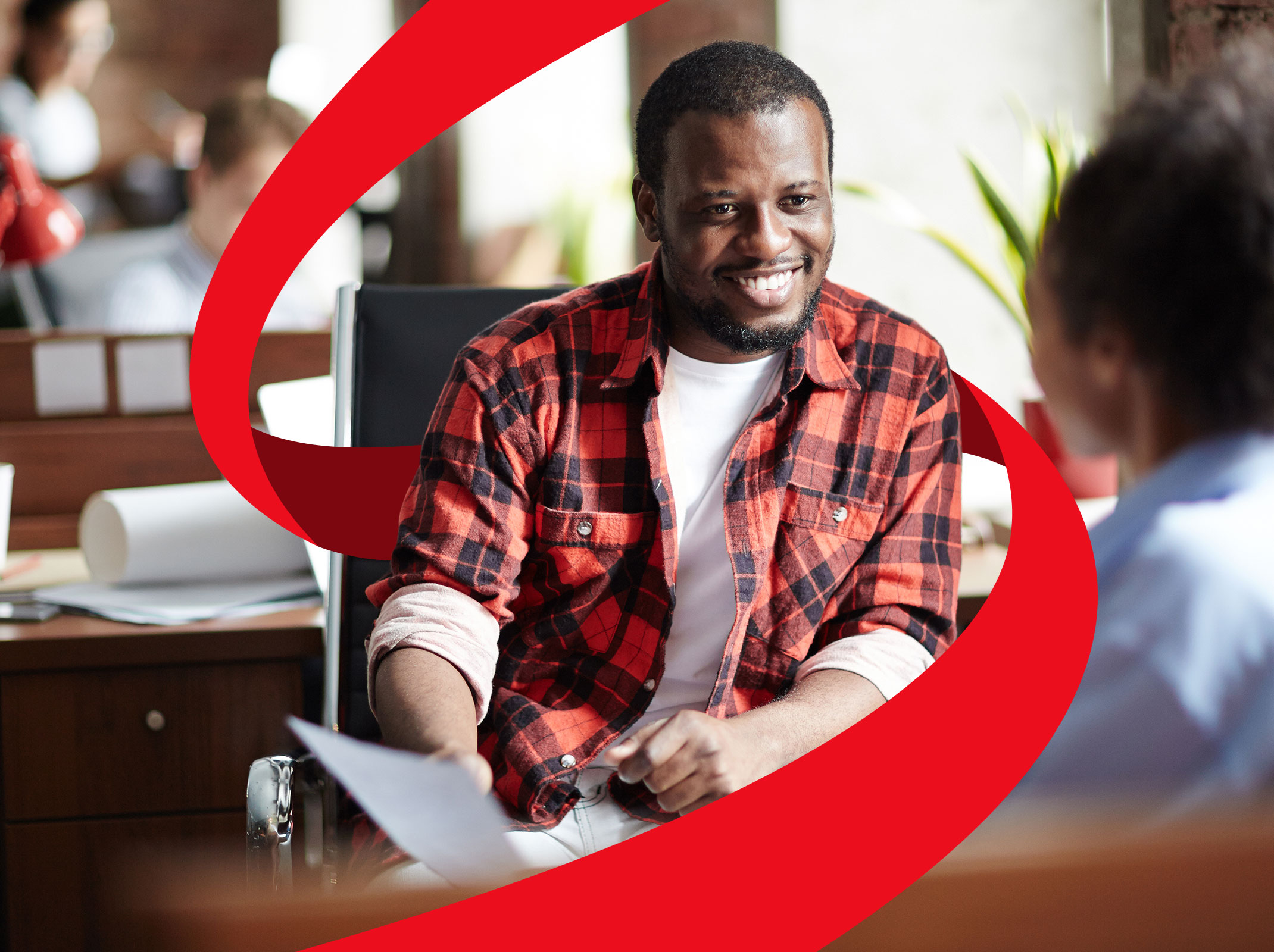 A leader giving performance feedback to an employee in an office setting. They are sitting at a desk with papers between them.